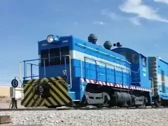Henderson Artificial Turf - A blue freight train with a striped yellow and black front moves along a gravel track under a bright blue sky, conveying a sense of motion and industrial strength.
