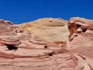 Henderson Artificial Turf - Colorful layered rock formations under a clear blue sky, showcasing shades of red, yellow, and beige in a natural landscape.