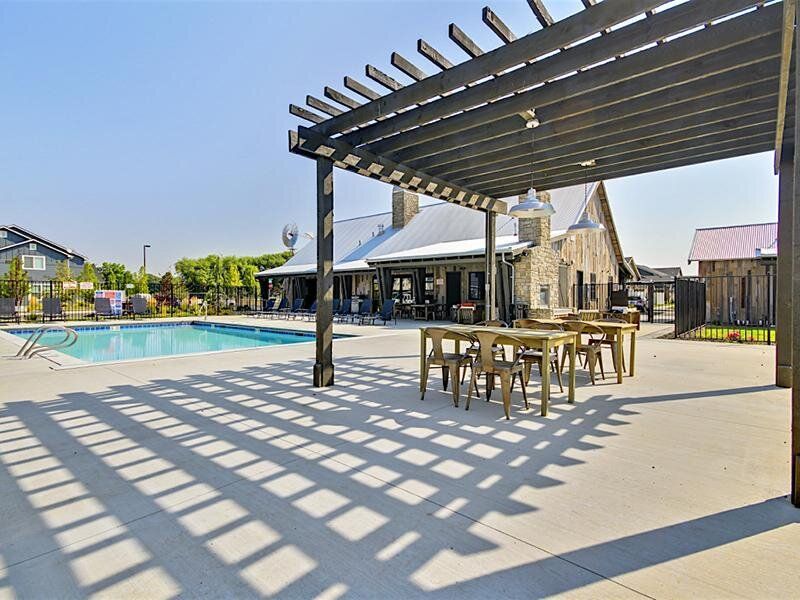 Poolside pergola with seating, stone building, pool, and clear sky.