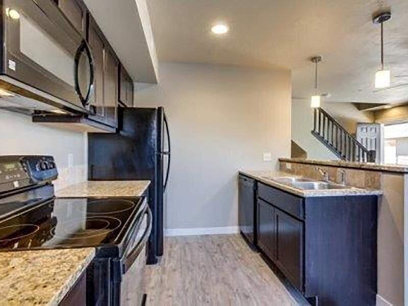 Kitchen with black appliances, granite countertops, light wood floors, and view of stairs.