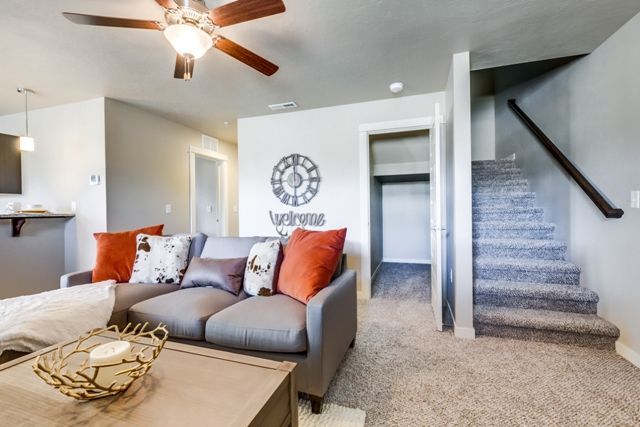 Cozy living room with gray couch, orange pillows, and stairs leading upwards.