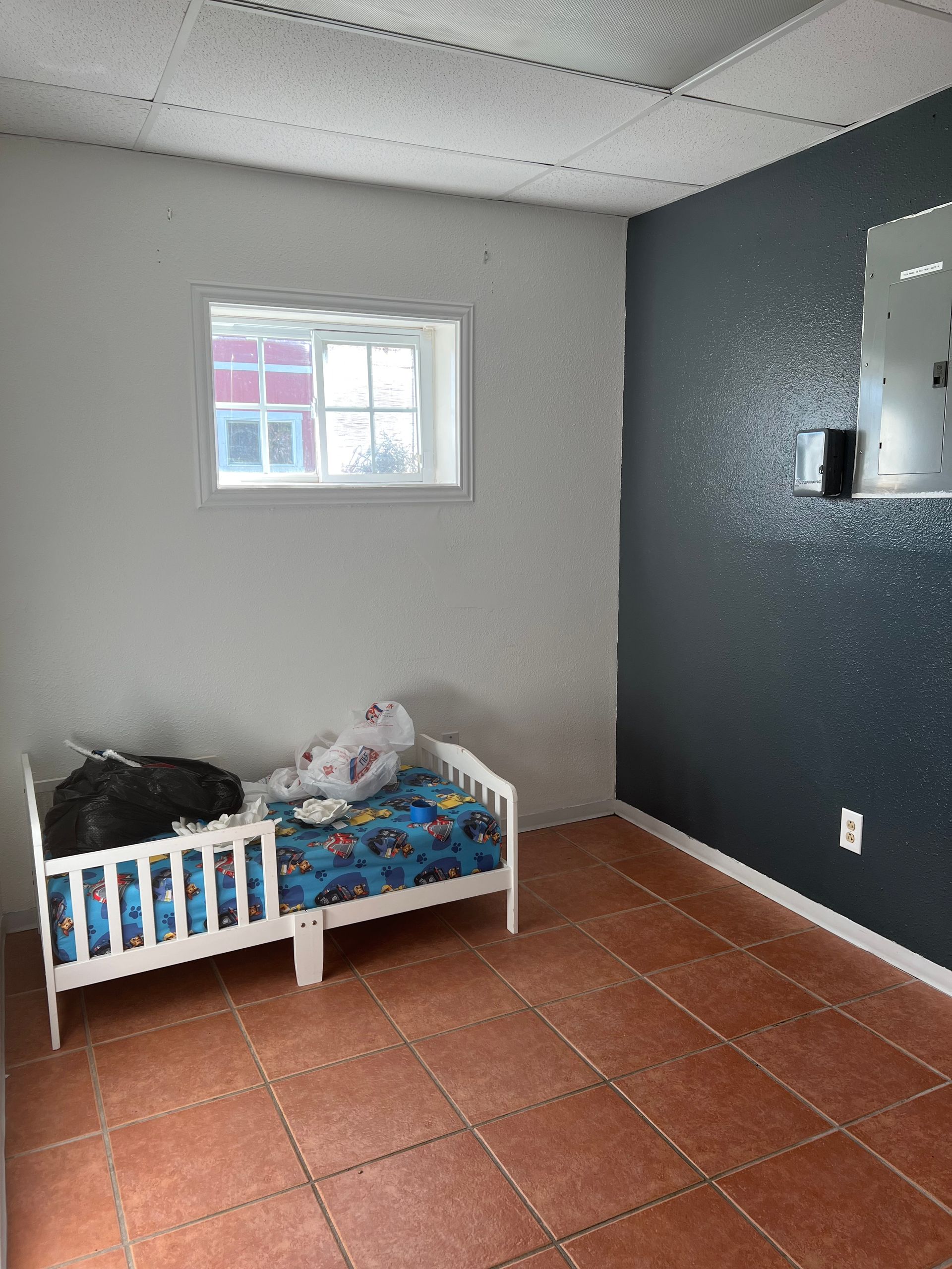 Child's bedroom with a small bed against a white wall, a blue accent wall, and a window.