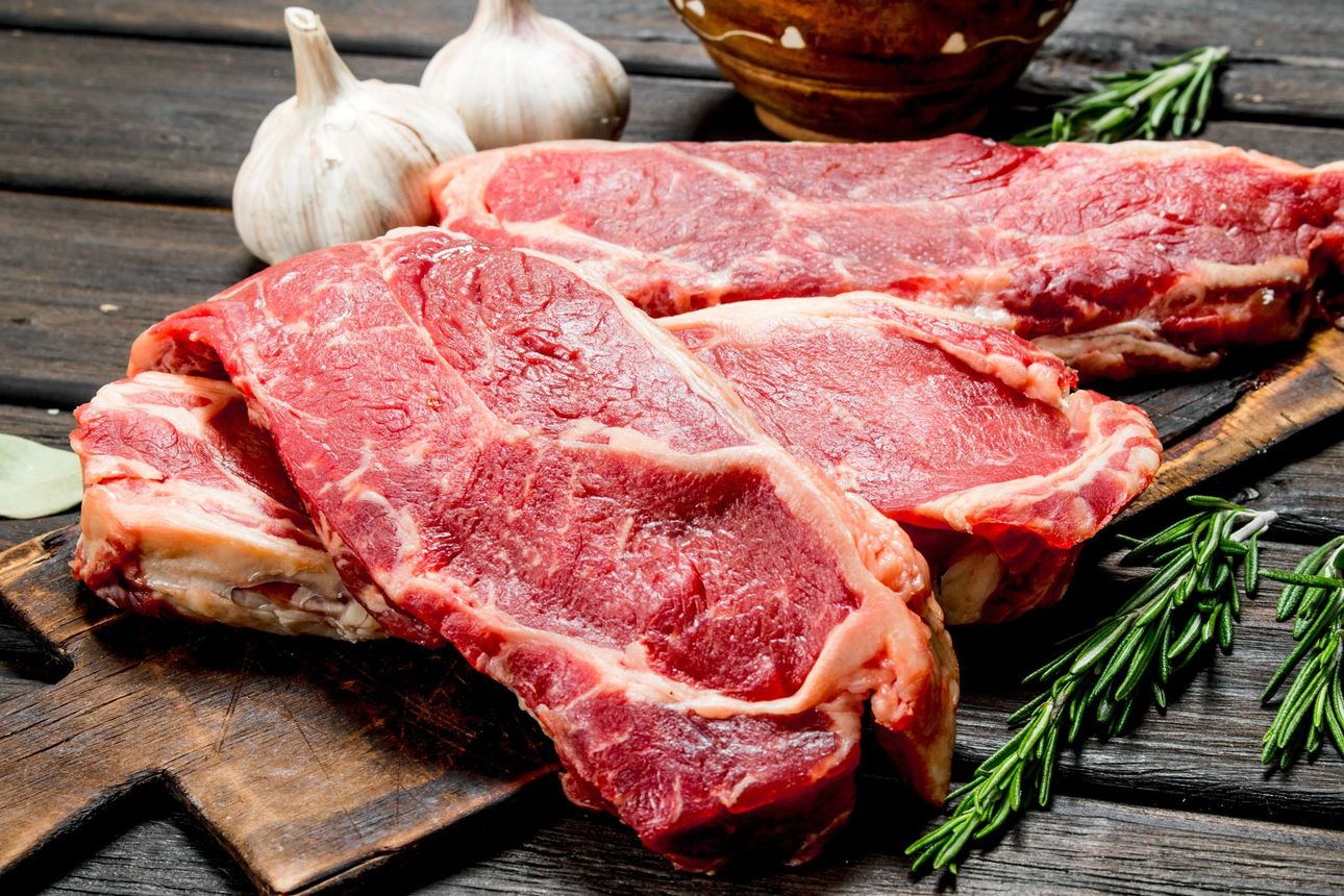 Filetes de ternera cruda, ajo, ramitas de romero sobre una tabla de cortar de madera, en un ambiente rústico.