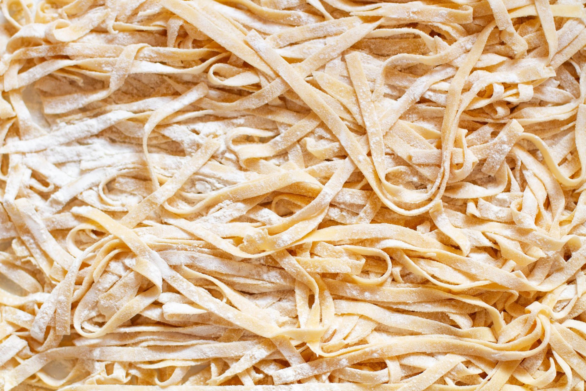 Pasta fettuccine fresca y cruda, de color beige claro, espolvoreada con harina.