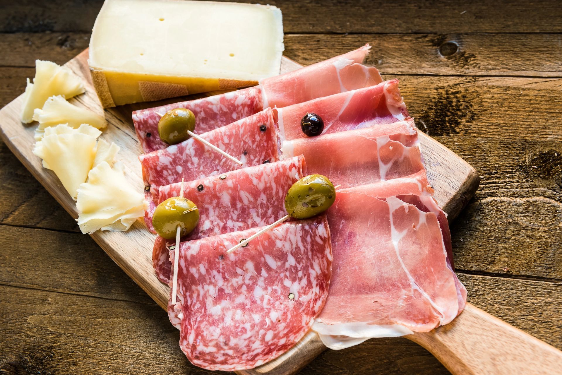 Tabla de embutidos con salami, prosciutto, queso y aceitunas sobre madera.