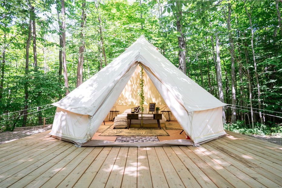 A white tent is sitting on top of a wooden deck in the middle of a forest.