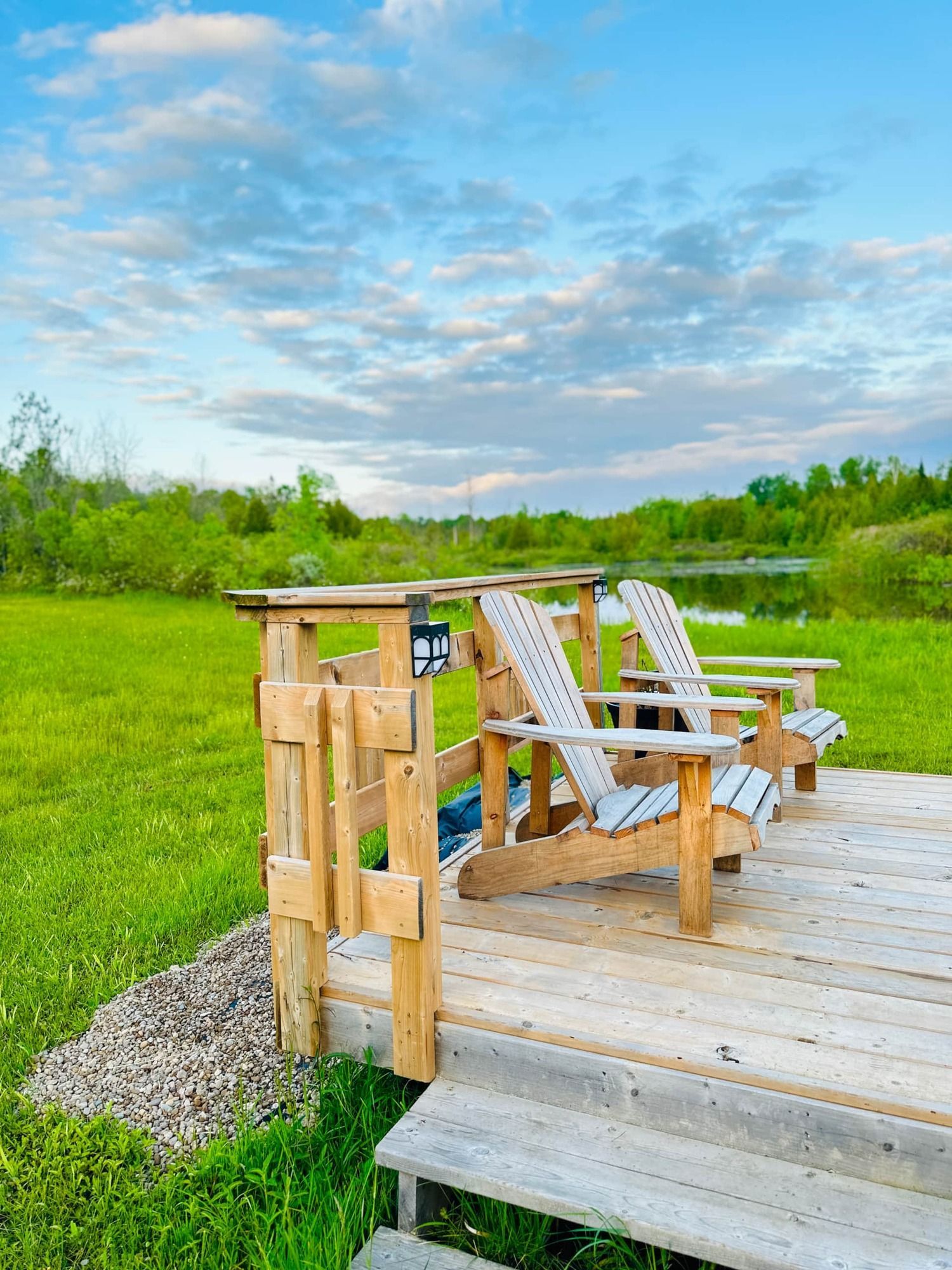 Two wooden chairs are sitting on a wooden deck overlooking a grassy field.