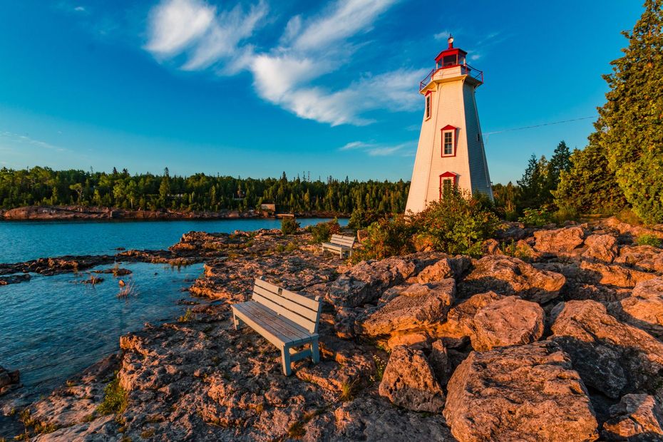 A lighthouse is sitting on a rocky shore next to a lake.