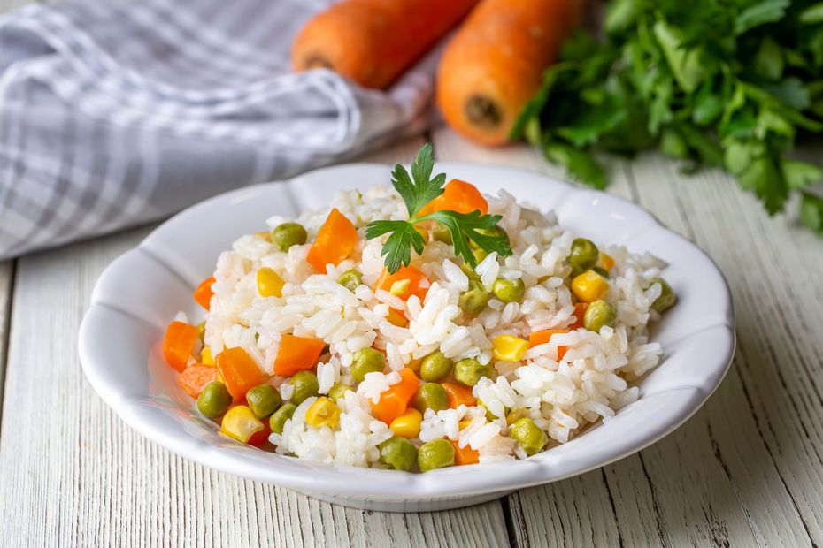 A white plate topped with rice , peas , carrots and corn.