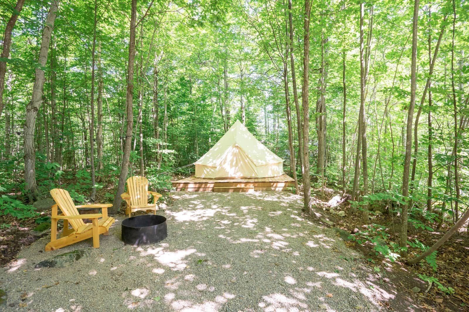 A tent is sitting in the middle of a forest next to a fire pit.