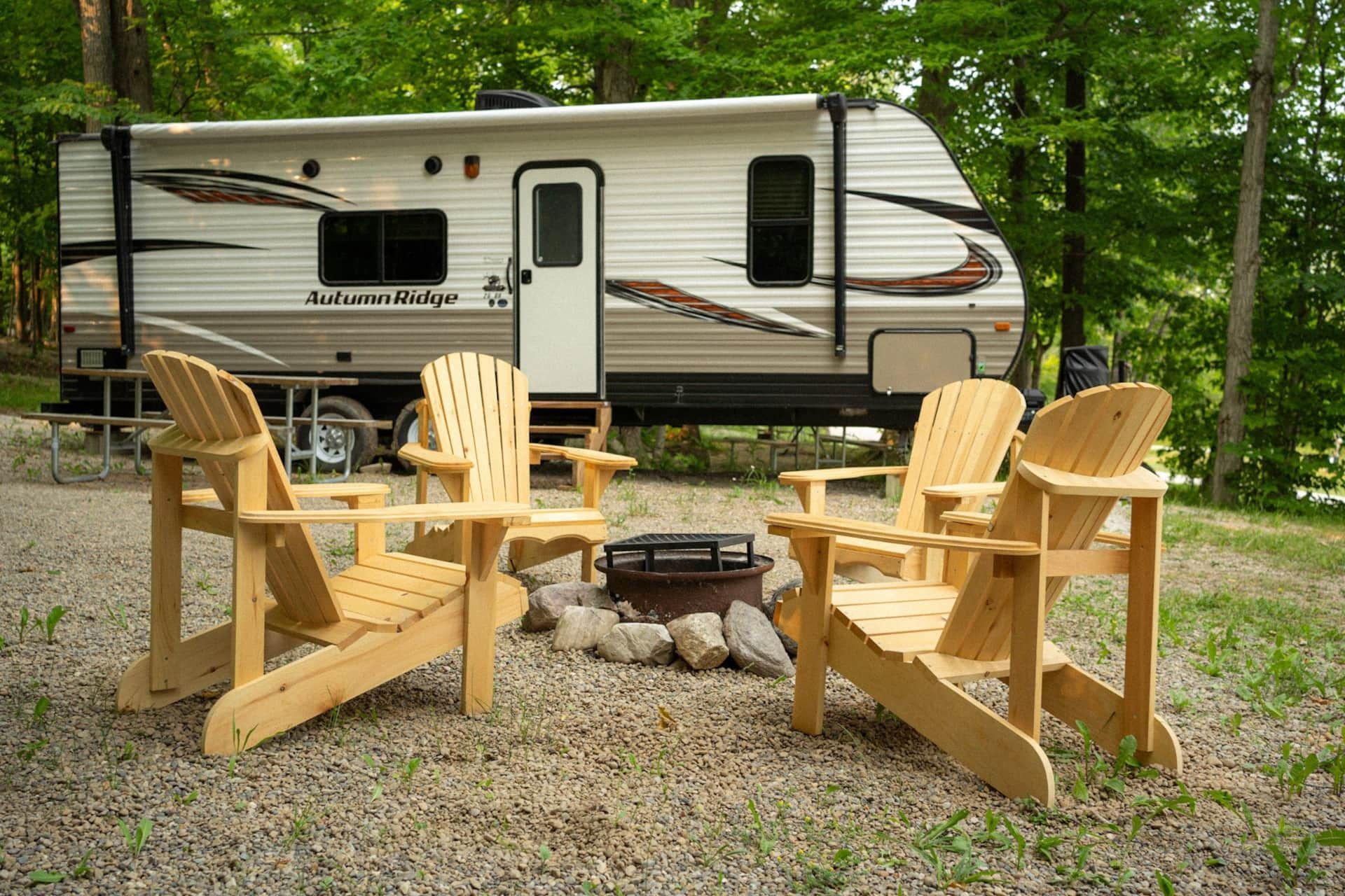 A rv is parked next to a fire pit and chairs.