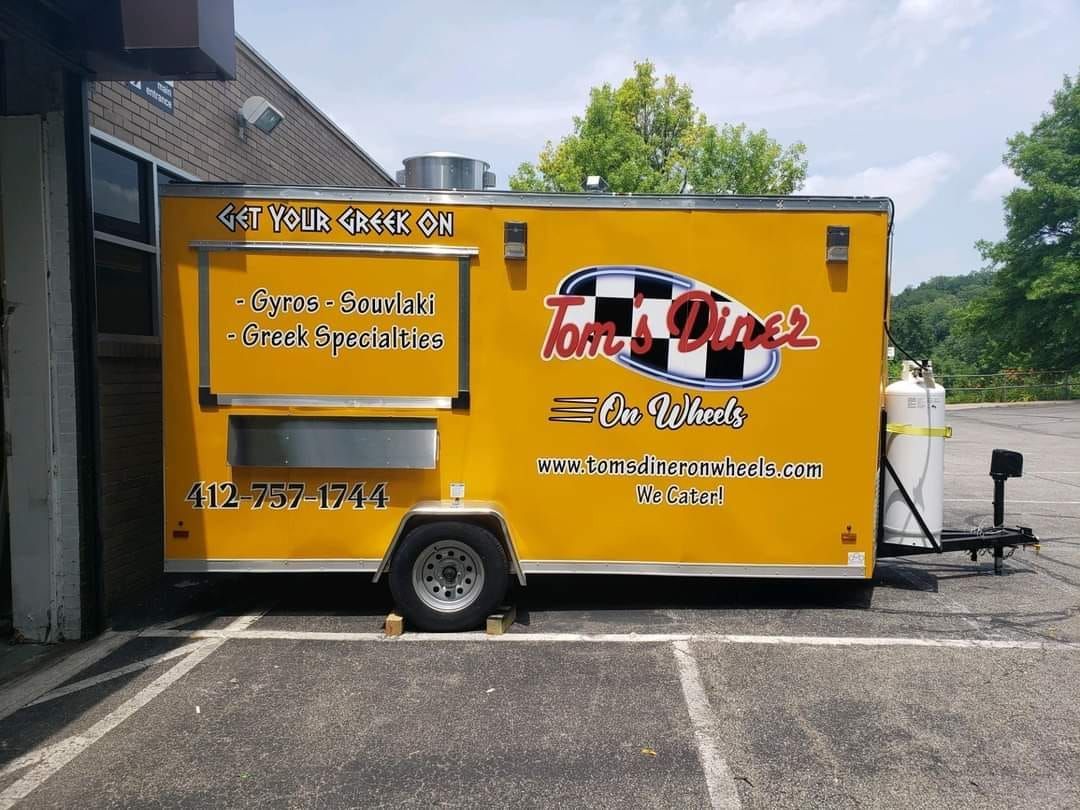Yellow Tom's Diner food truck with black and white checkered logo, parked outdoors.