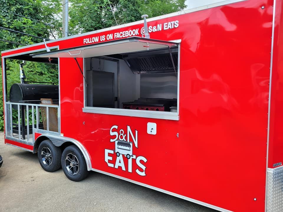 Red S&N Eats food trailer with an open service window and smoker on the side.