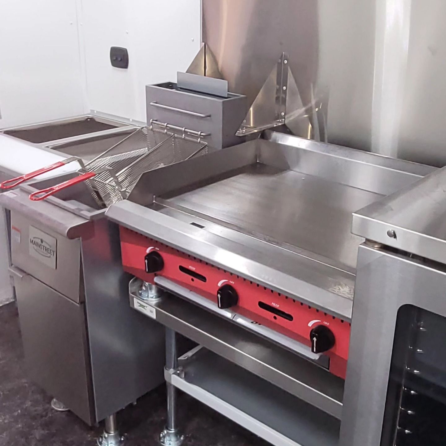 Stainless steel commercial kitchen equipment: grill, fryer, and oven.