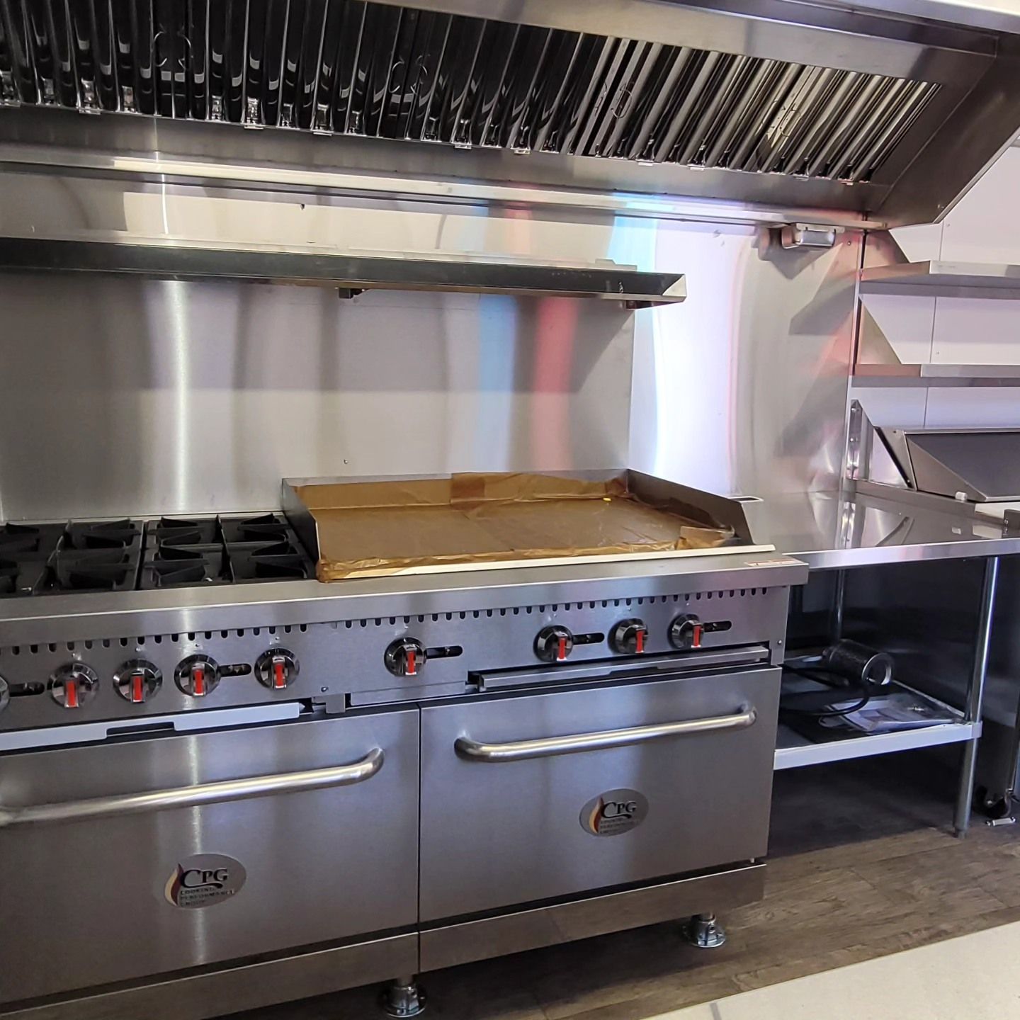 Stainless steel commercial kitchen with a stove, grill, and range hood.