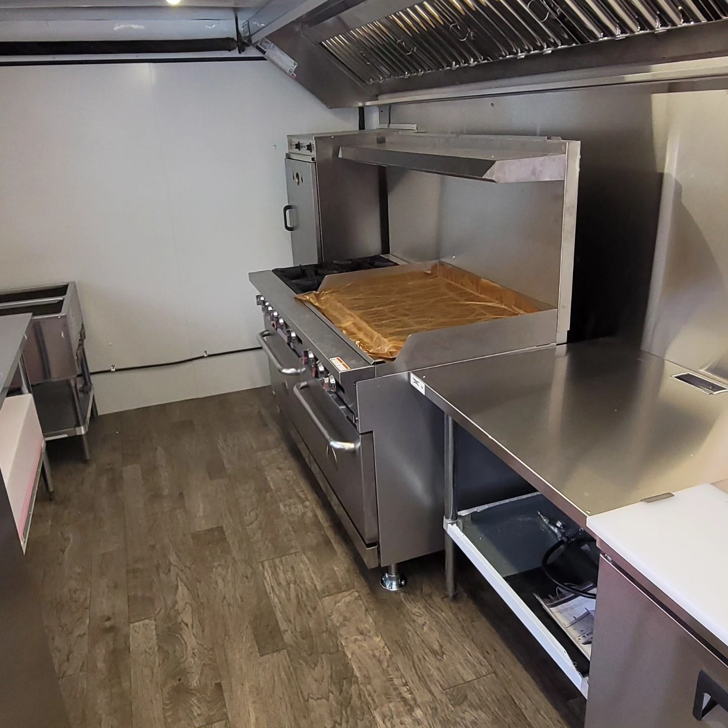 Interior view of a food truck kitchen with a stainless steel range, exhaust hood, and countertop.