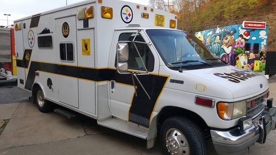 White ambulance with black and gold accents; Steelers logo; parked outside.
