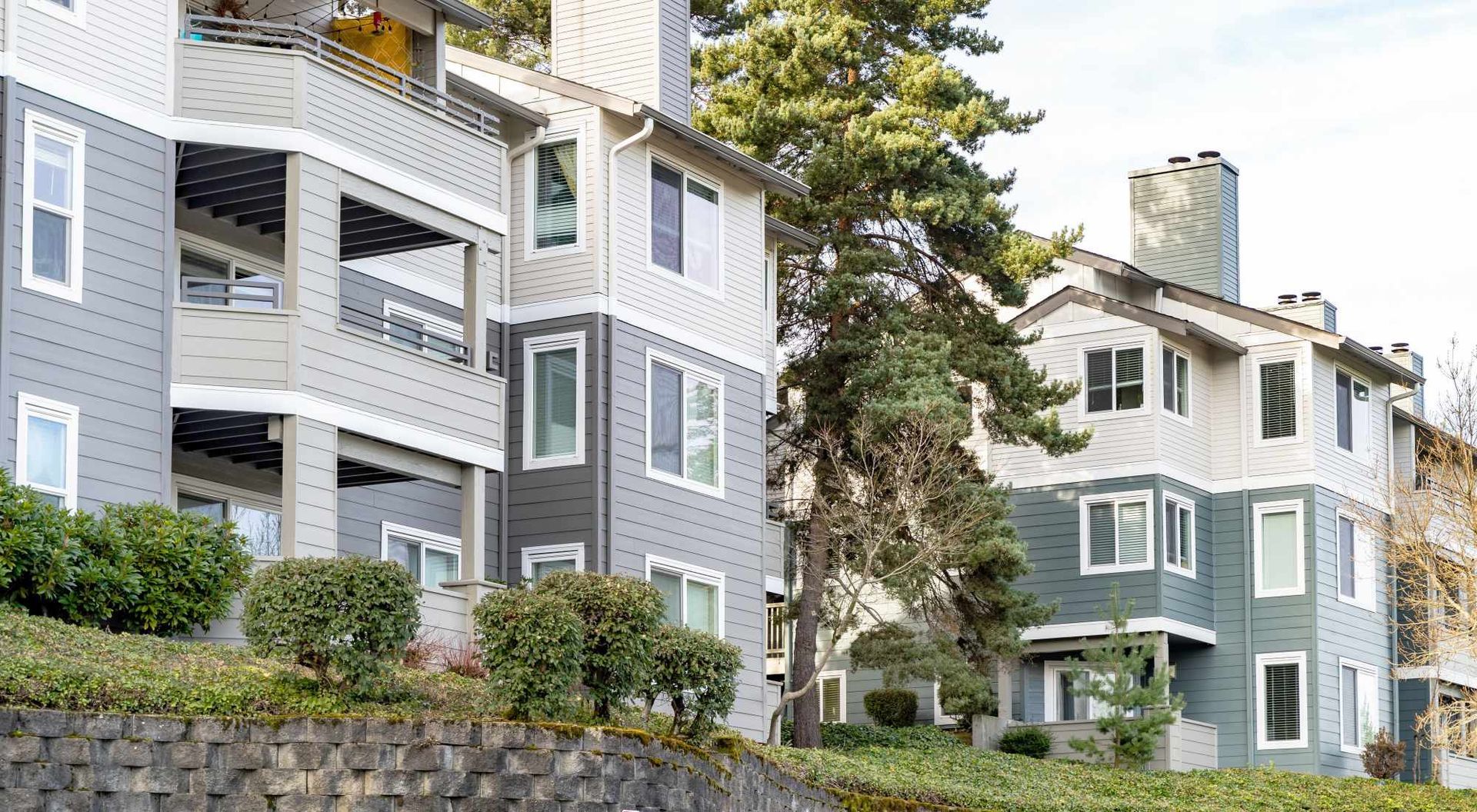 Exterior view of a multi-story apartment building with stacked balconies and landscaped hillside.