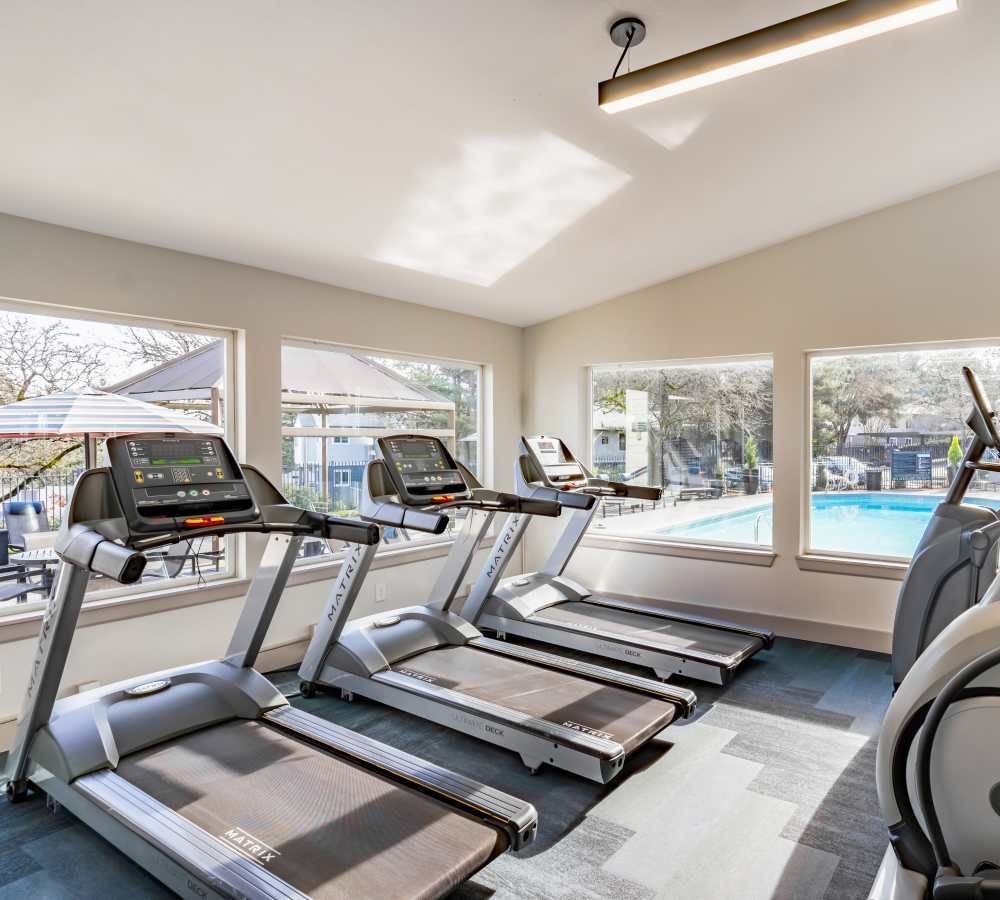 Bright fitness center with several treadmills and large windows overlooking the outdoor pool.