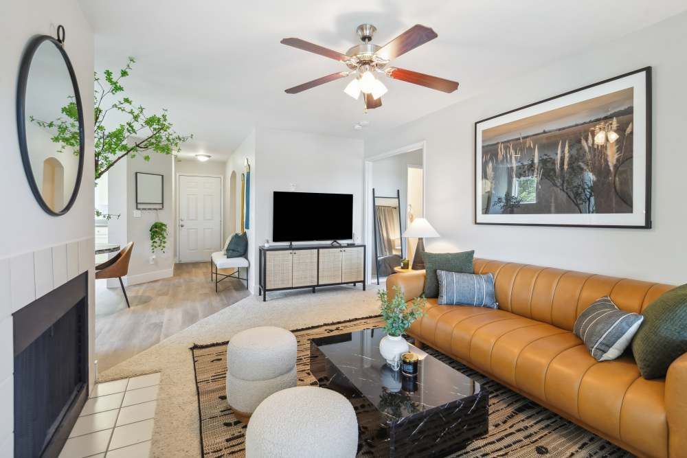 Living room with a tan leather sofa, black coffee table, TV, ceiling fan, and wall art.