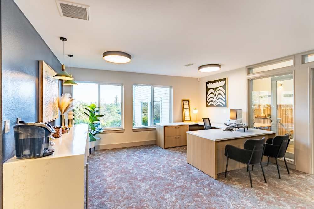 Interior leasing office with desk, chairs, cabinets, plants, and large windows.