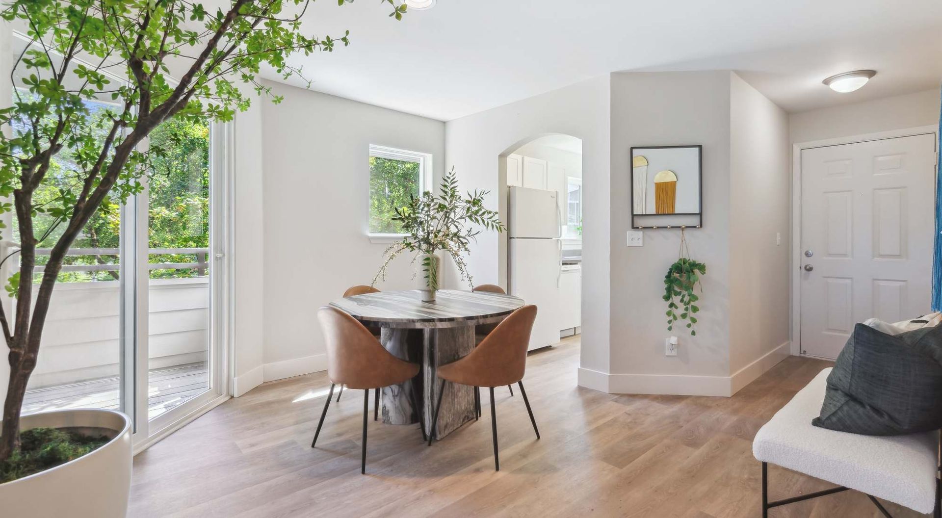 Dining area with round marble table, brown chairs, large sliding door to balcony, and an indoor plant nearby.