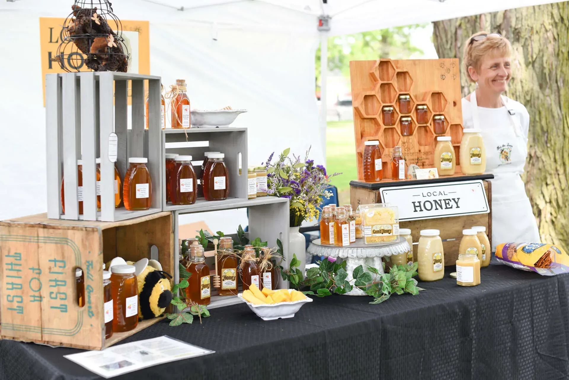 A woman is standing in front of a table full of jars of honey.