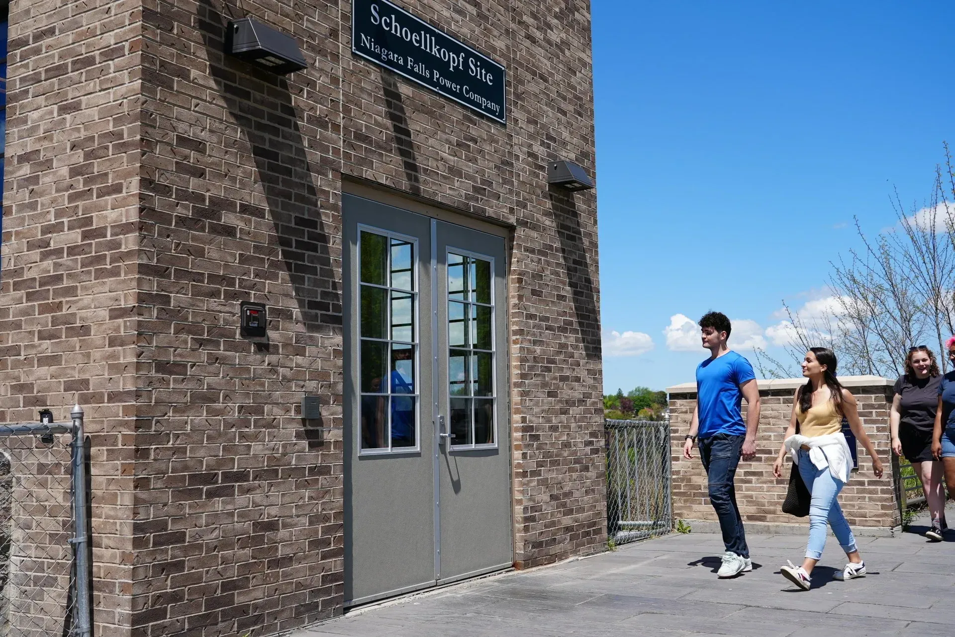 A group of people are walking in front of a brick building.