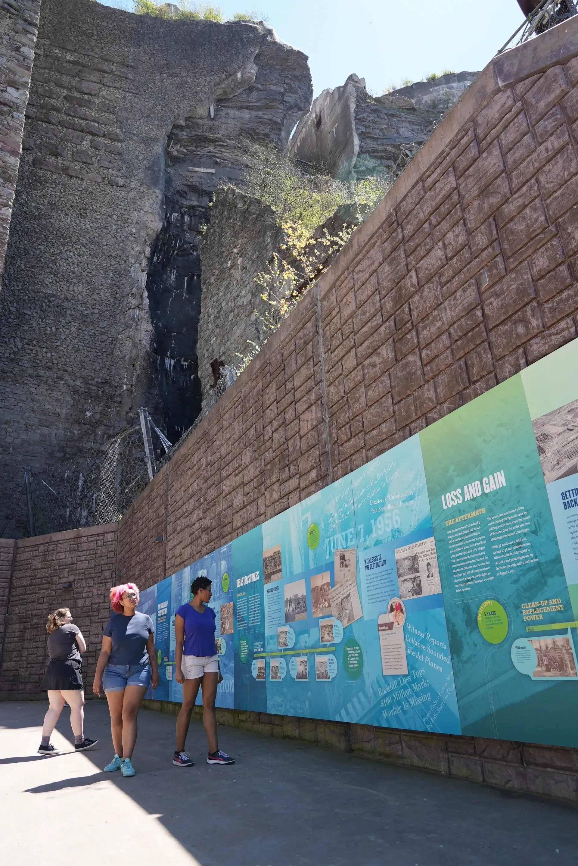 A group of people are standing in front of a large brick wall.
