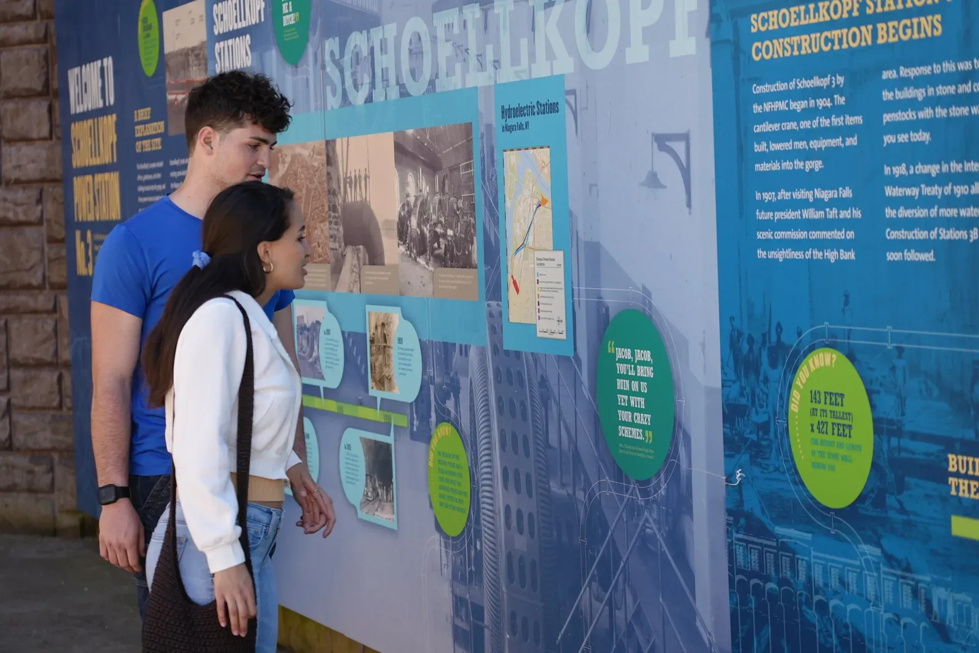 A man and a woman are looking at a display on a wall.