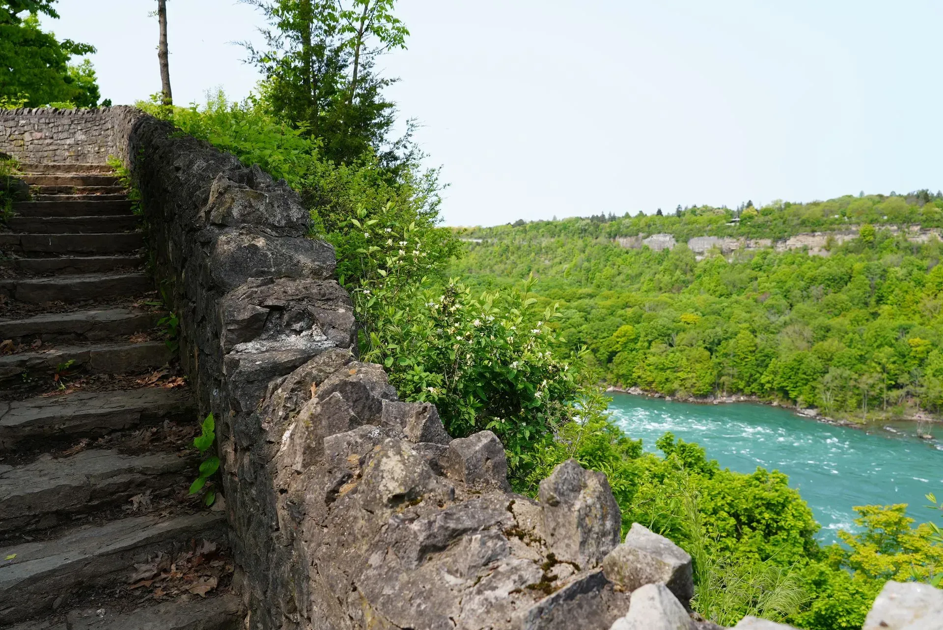 A stone wall with stairs leading up to a river surrounded by trees.