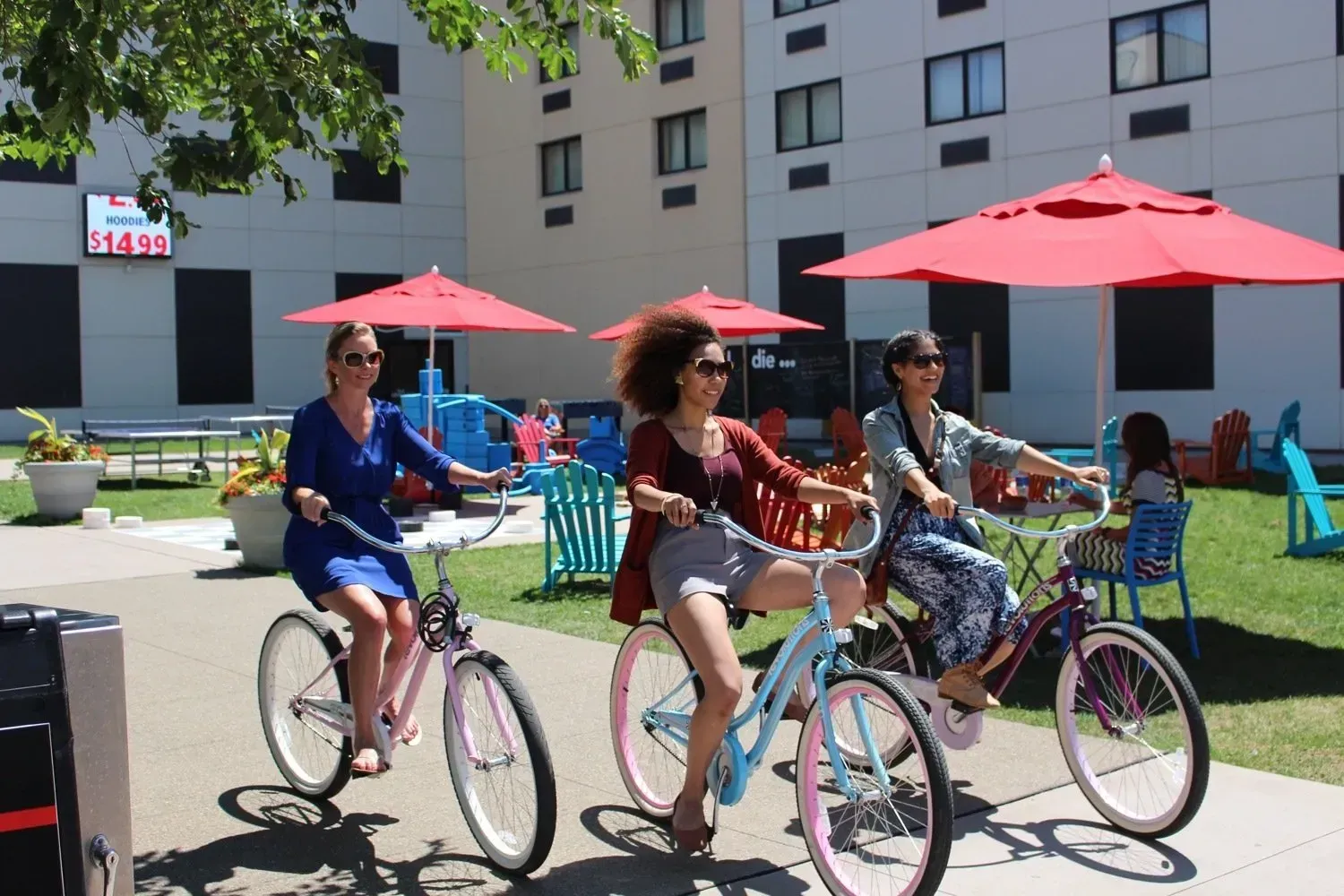 Three women are riding bicycles on a sidewalk under red umbrellas