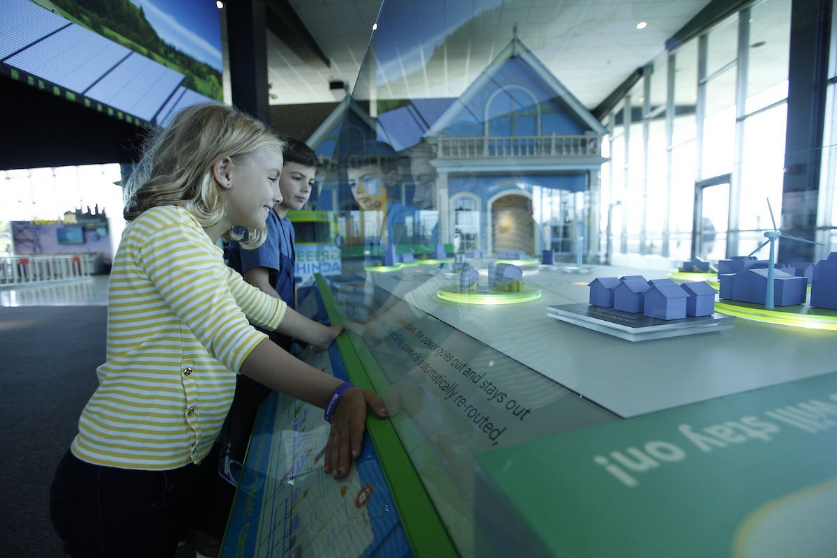 A boy and a girl are looking at a model of a house on a table.