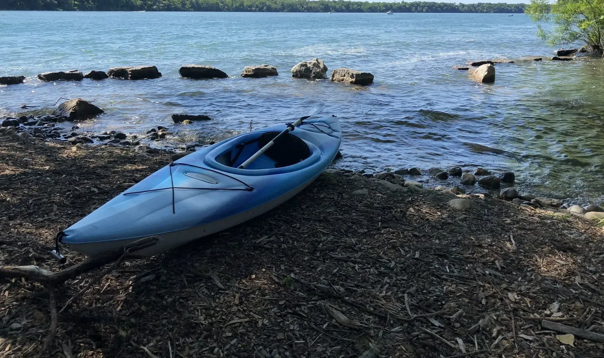 A blue kayak is sitting on the shore of a lake.