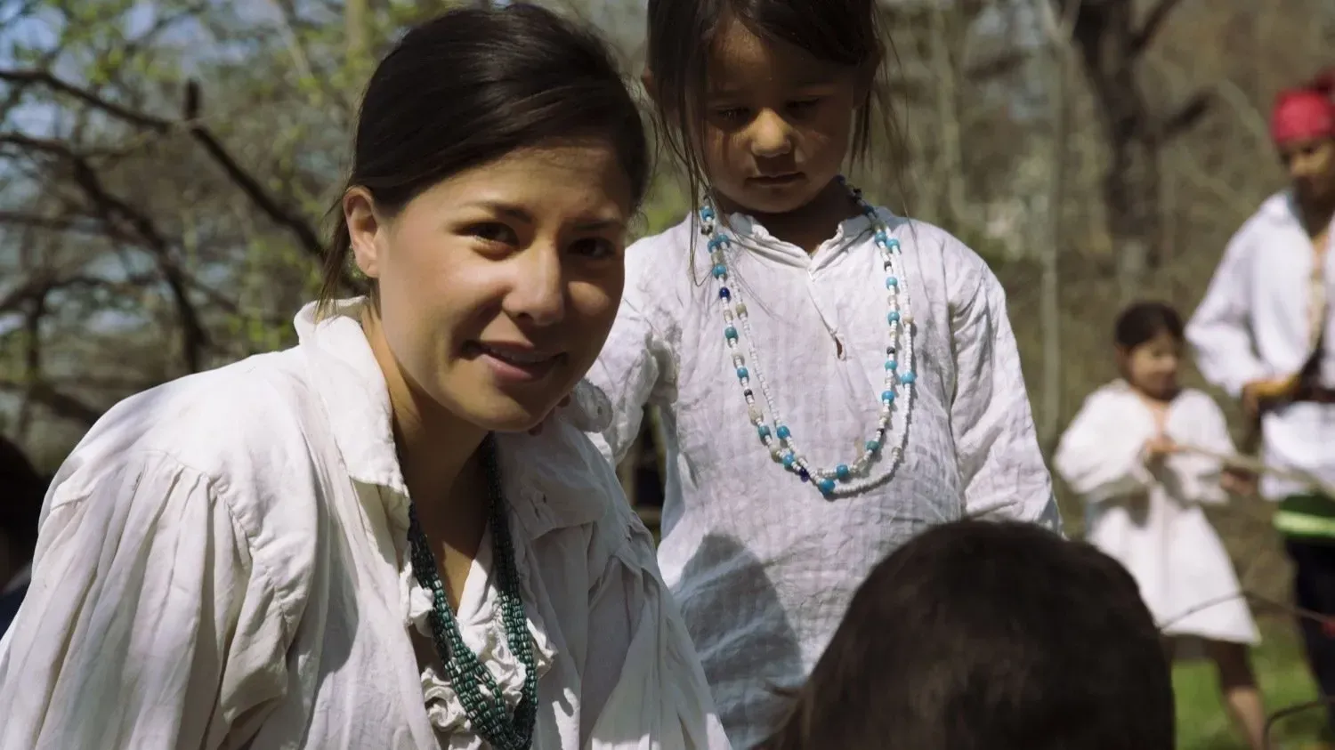 A woman in a white shirt is standing in front of a group of children.