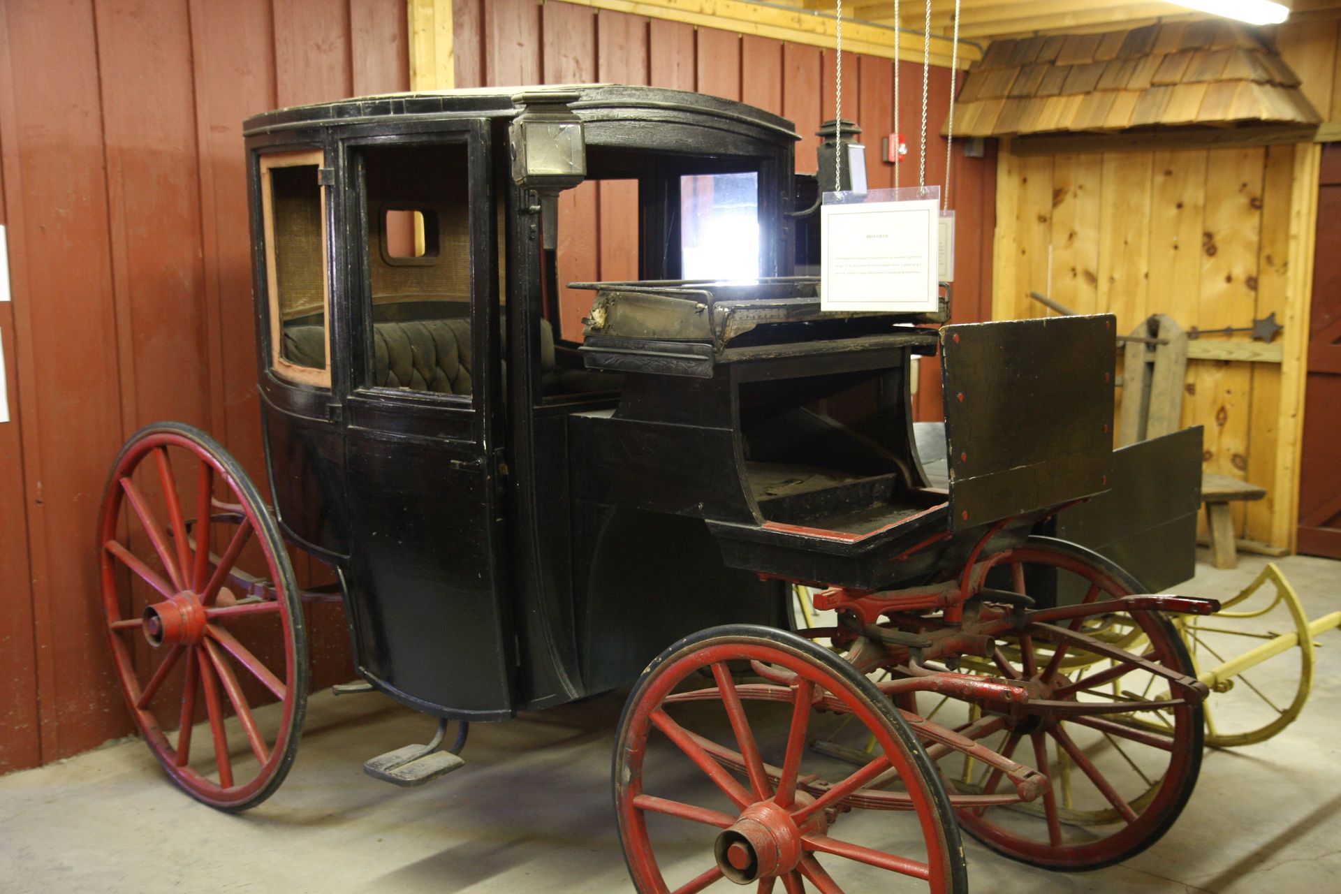 A black horse drawn carriage with red wheels is parked in a garage.