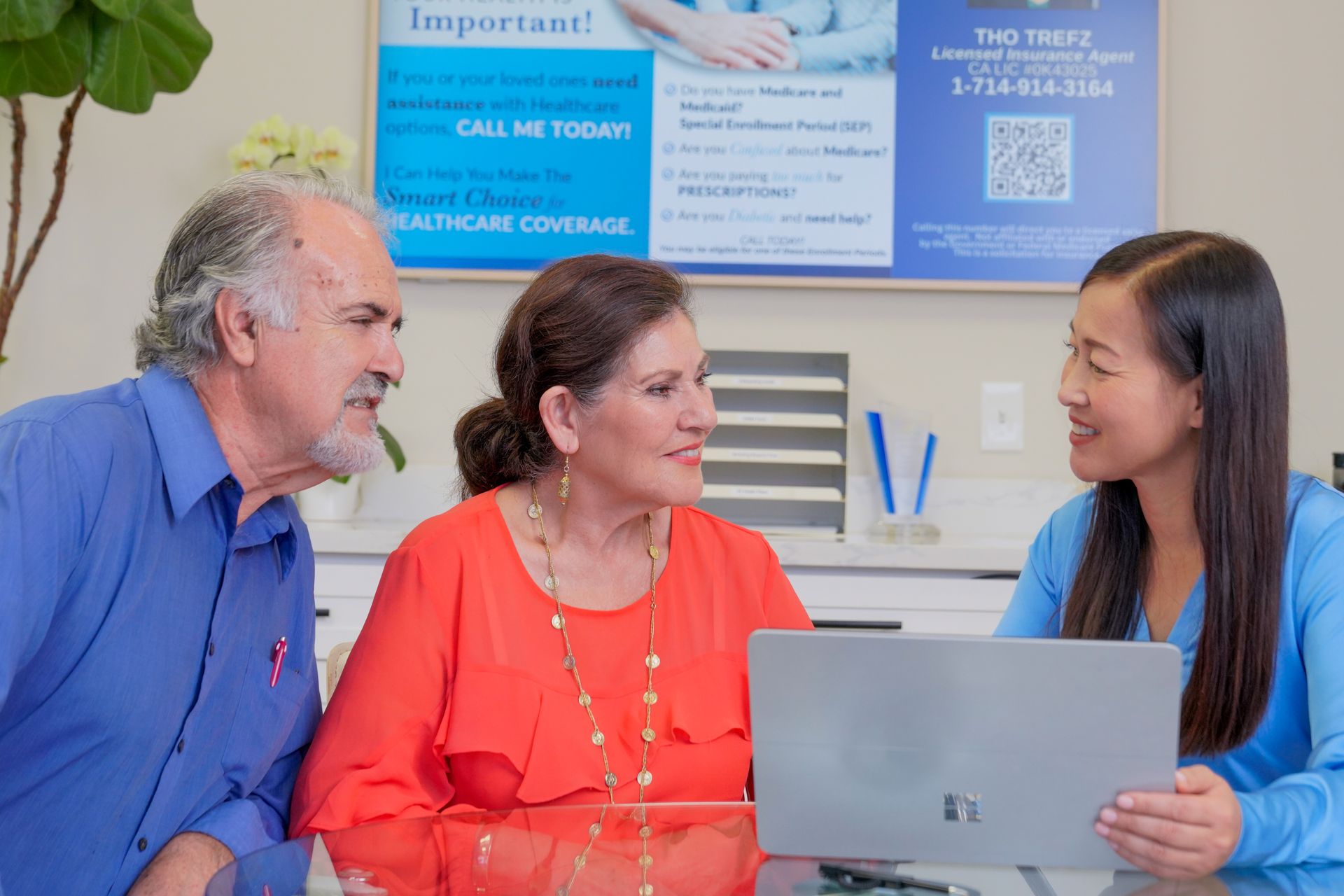 Family sitting on the floor laughing. A sofa and plants are in the background.