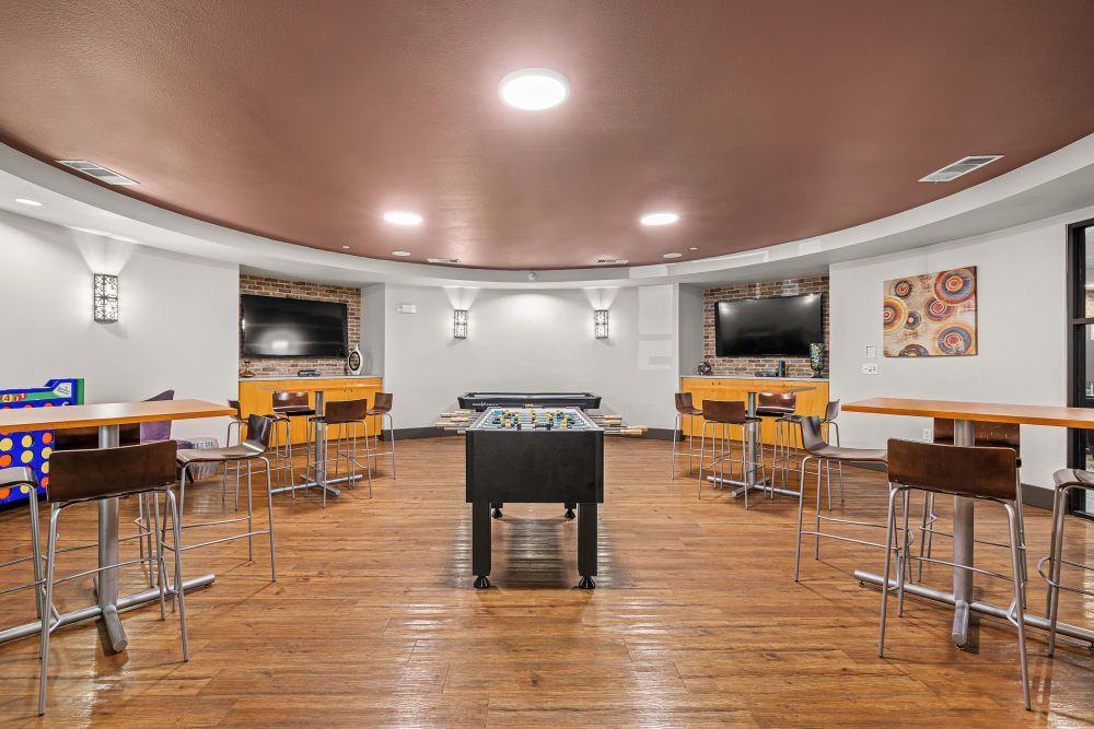 Apartment game room with tables and chairs and a foosball table at Regents West at 26th in Austin, TX, near UT Austin.