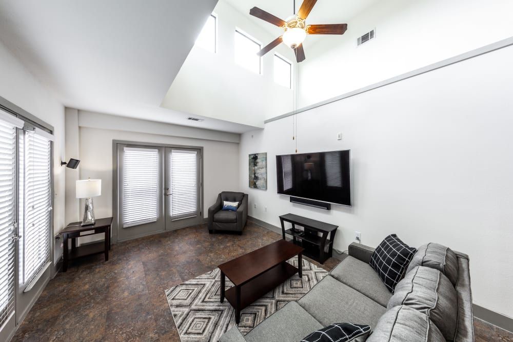 Apartment living room with a couch, chair, coffee table, television, and ceiling fan at Regents West at 26th in Austin, TX, near UT Austin.