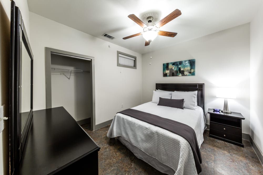 Apartment bedroom with a bed, nightstand, mirror, and ceiling fanat Regents West at 26th in Austin, TX, near UT Austin.