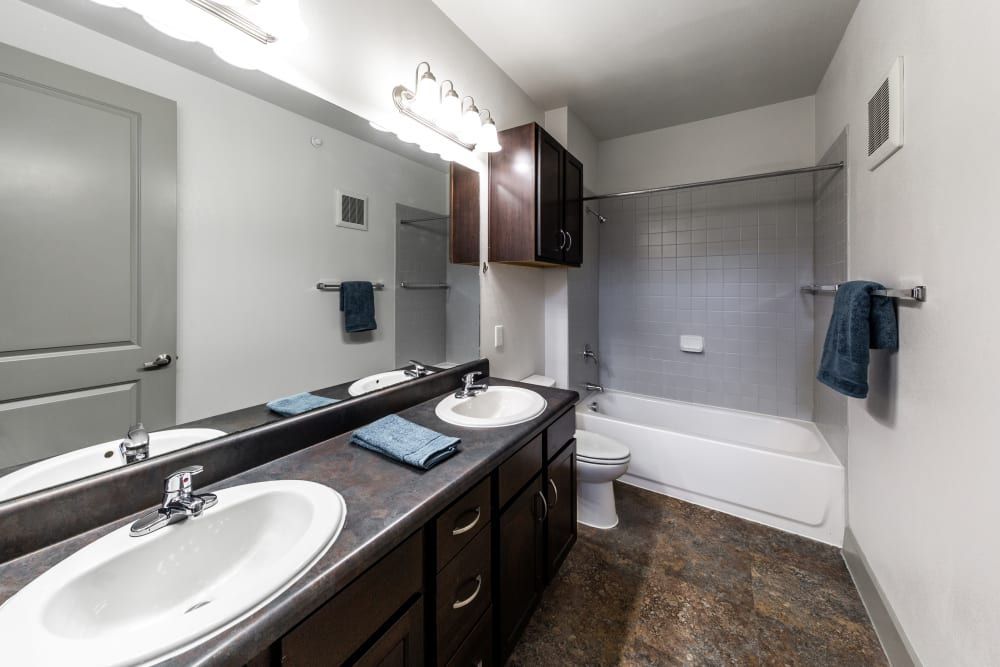 Student apartment bathroom with two sinks, a toilet, and a bathtub at Regents West at 26th in Austin, TX, near UT Austin.