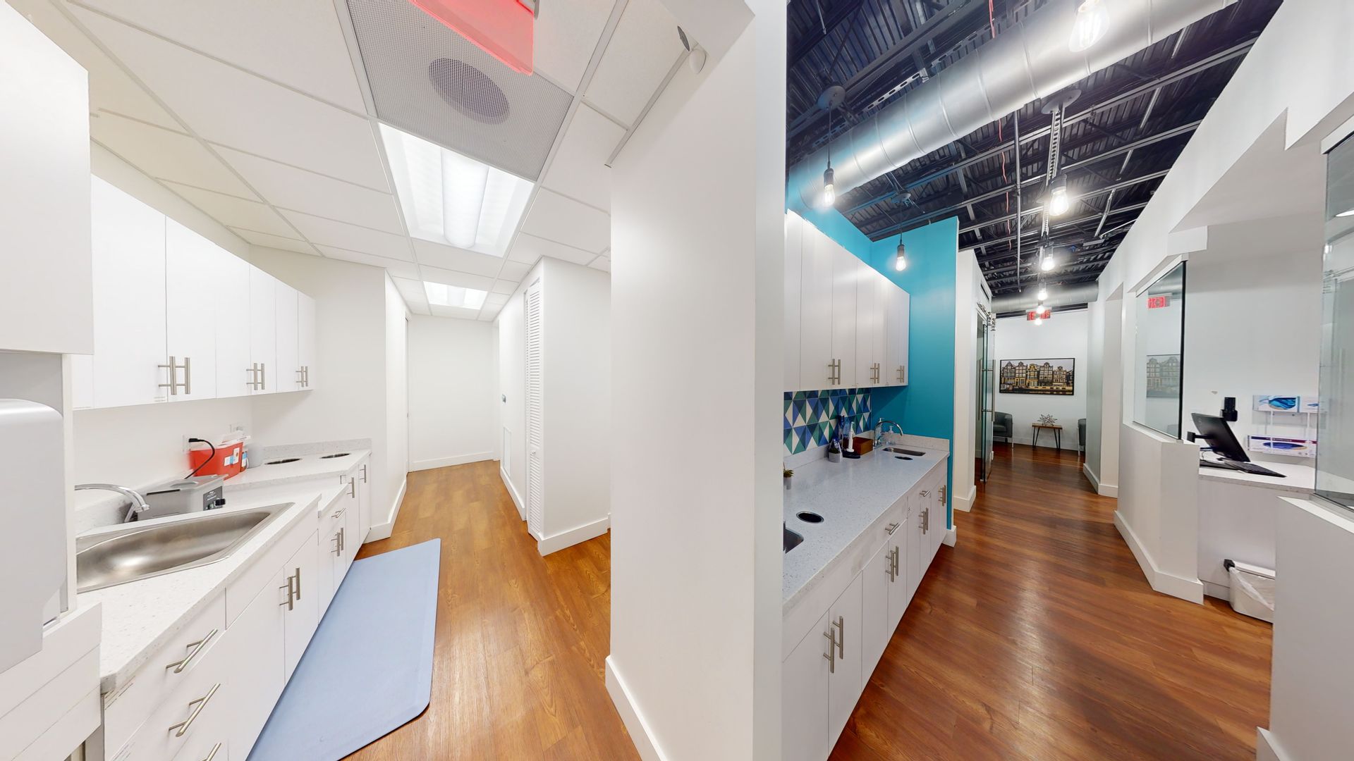 A kitchen with white cabinets and wooden floors in a hallway.