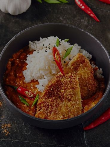 Bowl of Japanese curry with rice, two breaded cutlets, and red chili peppers.