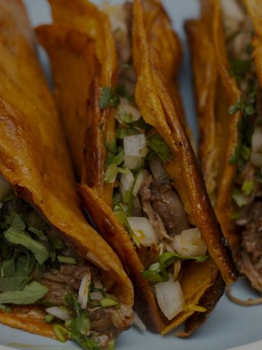 Close-up of crispy tacos filled with meat, onions, and cilantro.