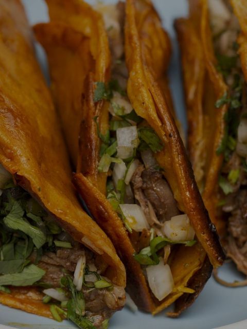 Close-up of crispy tacos filled with meat, onions, and cilantro.