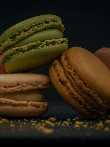 Stack of colorful macarons, including green, tan, and brown, on a dark surface.