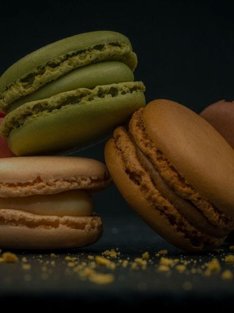 Stack of colorful macarons, including green, tan, and brown, on a dark surface.