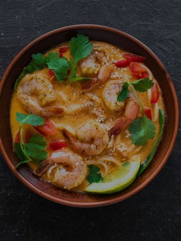 Shrimp coconut curry soup with herbs and lime in a wooden bowl on a dark surface.