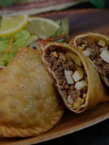 Fried empanada with beef, egg, and salad on a wooden plate.