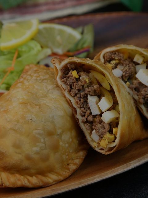 Fried empanada with beef, egg, and salad on a wooden plate.